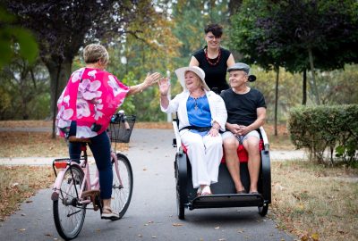 na zdjęciu rowerzystka wiezie dwóch pasażerów na rikszy